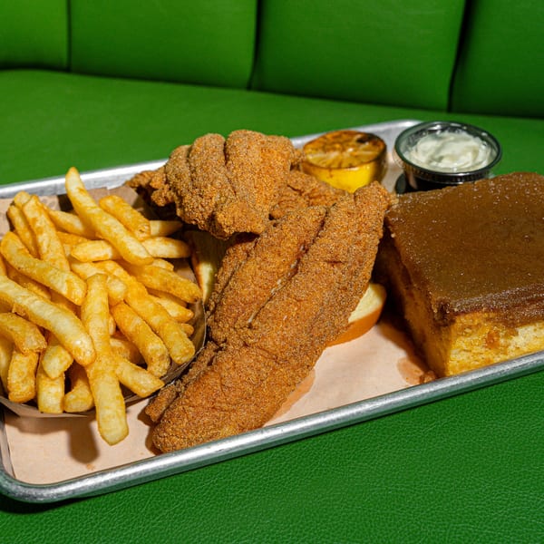 Fried catfish, french fries, cornbread, tartar sauce, and grilled lemon on a metal tray.