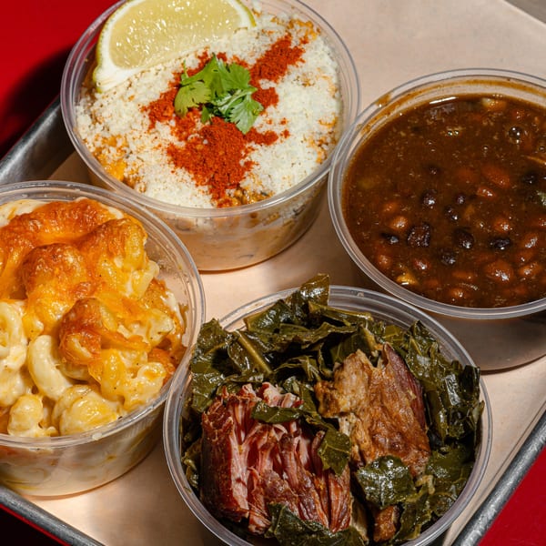 Four clear containers of Sanders BBQ sides: mac and cheese, collard greens, elote, and black beans.