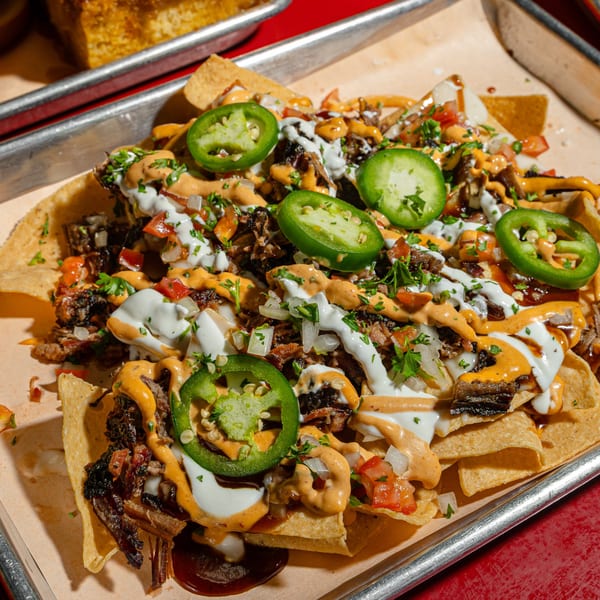 Sanders BBQ Co. nachos with pulled pork, jalapeños, pico de gallo, and creamy sauces on a tray.